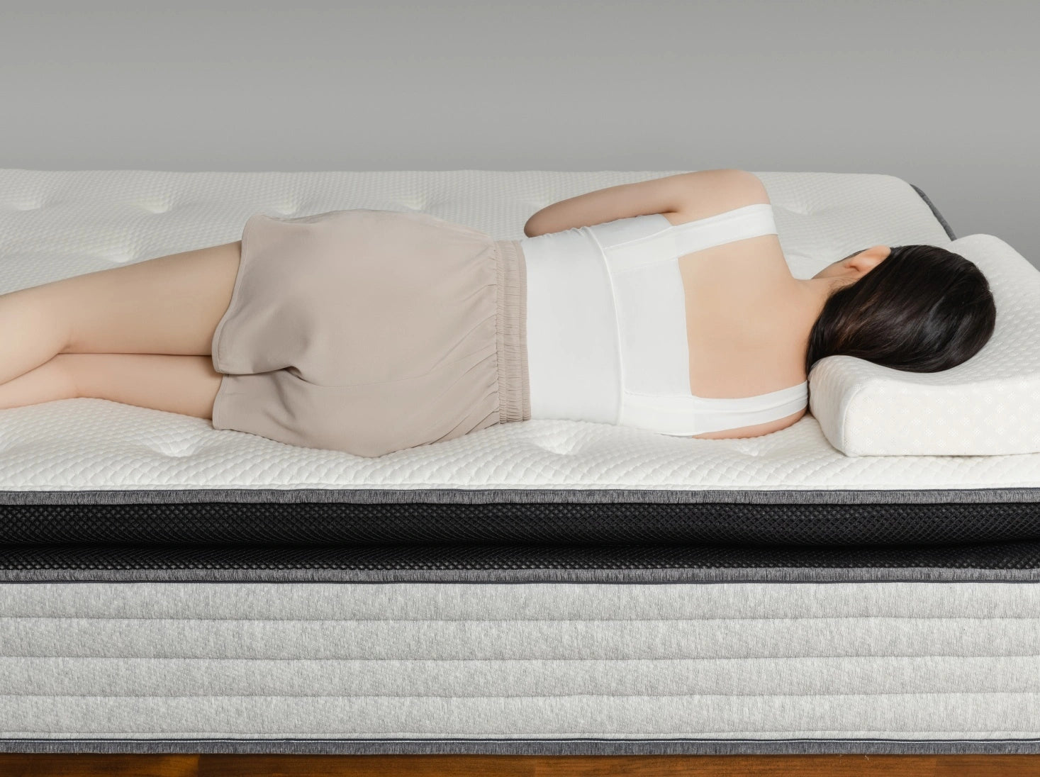 一位女性側躺在 Premium 2.3 零壓深眠床墊上,身體自然貼合床面曲線,展現床墊支撐與釋壓效果。床墊採用白色立體菱格紋天絲表布,搭配黑色透氣網布中層與灰色橫紋針織側邊,構成豐富層次感。整體氛圍靜謐柔和,傳遞放鬆沉睡的安心感受。