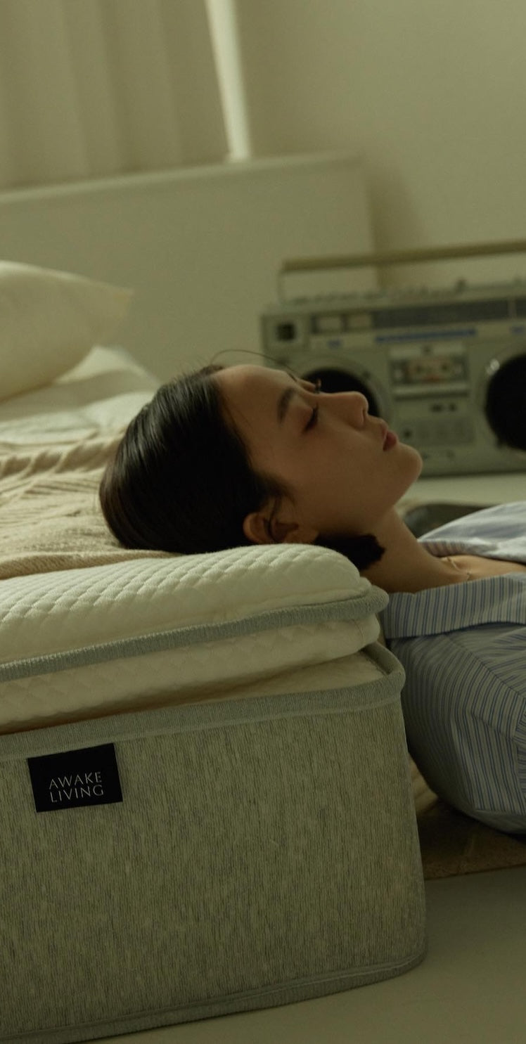 一位女性頭枕在床墊上閉眼休息,前景是 Awake Living 床墊的品牌布標。