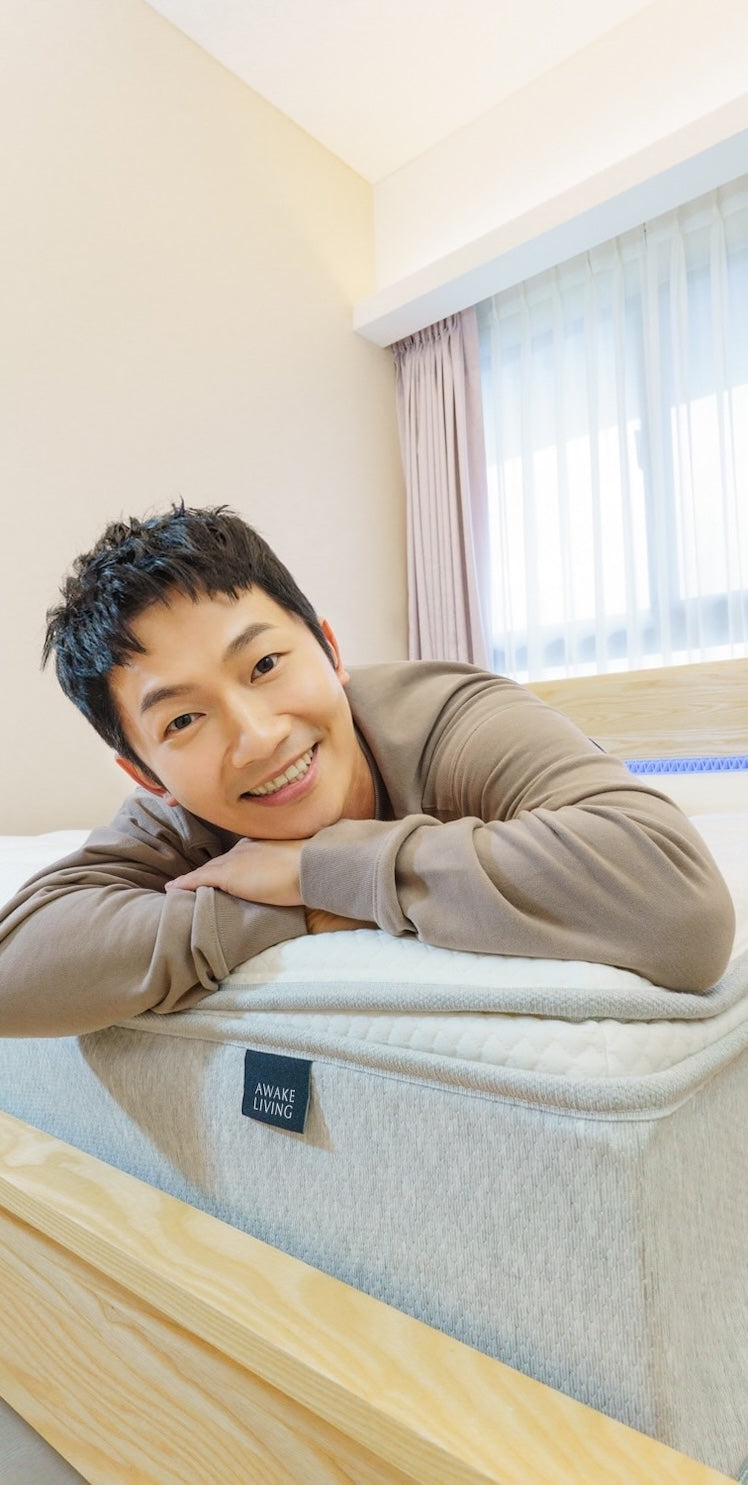 一位面帶微笑的男性趴在床墊上,前景清楚地顯示 Awake Living 品牌布標。