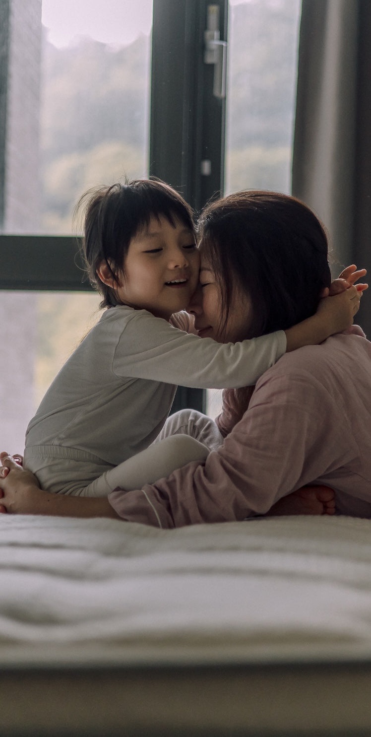 一位母親與孩子在白色的床上相互擁抱,背後是明亮的窗戶。