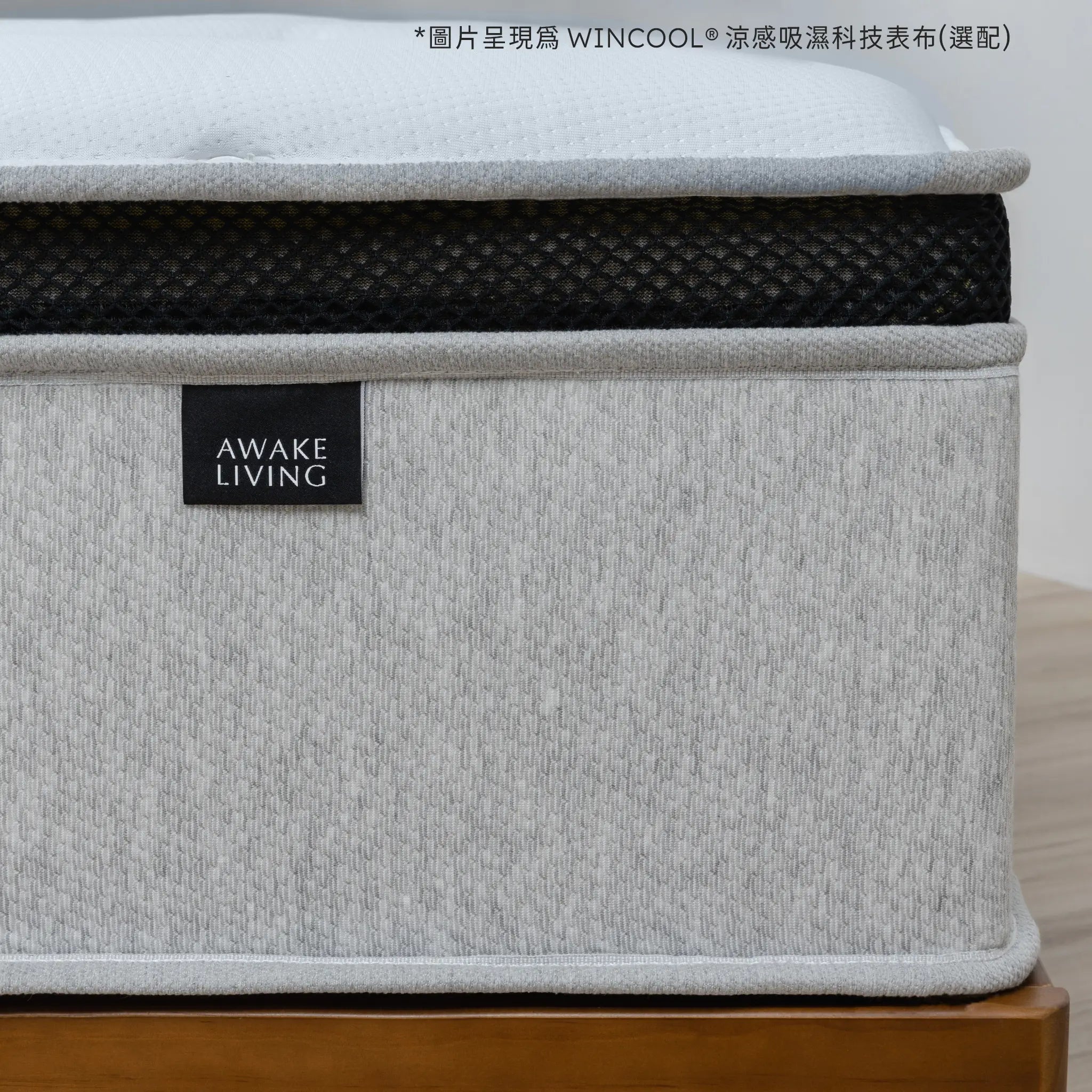 Firm 2.3 床墊的側面特寫,聚焦於品牌布標、灰色床邊與黑色網眼飾帶。