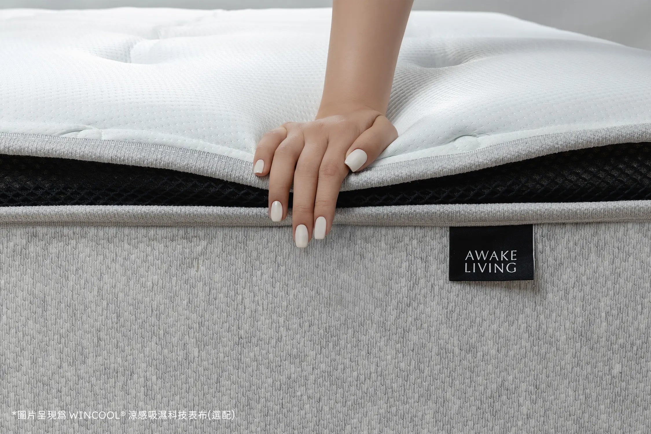 手掌輕壓 Firm 2.3 沈睡四季床墊表層,展現床墊紮實支撐與表布柔軟觸感,搭配 WINCOOL® 涼感吸濕科技表布,帶出清爽舒眠的使用體驗。黑色透氣層與灰色包覆布料營造層次對比,AWAKE LIVING 品牌標籤簡約點綴於側邊,呈現清新現代的設計語彙。