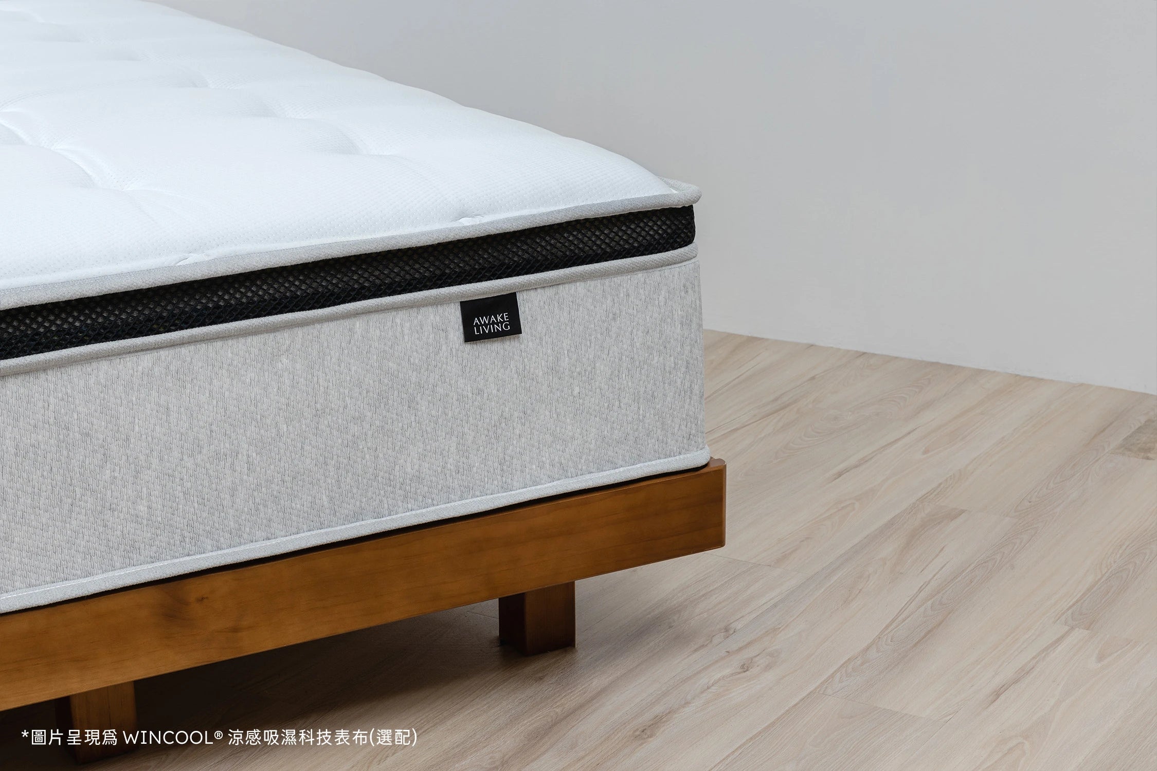 Firm 2.3 沈睡四季床墊置於原木床架上,畫面展現床墊厚實側邊結構與清爽淺灰色調,搭配選配的 WINCOOL® 涼感吸濕科技表布,強調舒適與涼爽的睡眠體驗。黑色透氣網布層與品牌標籤 AWAKE LIVING 輕巧點綴其上,襯托出極簡而具質感的現代居家氛圍。