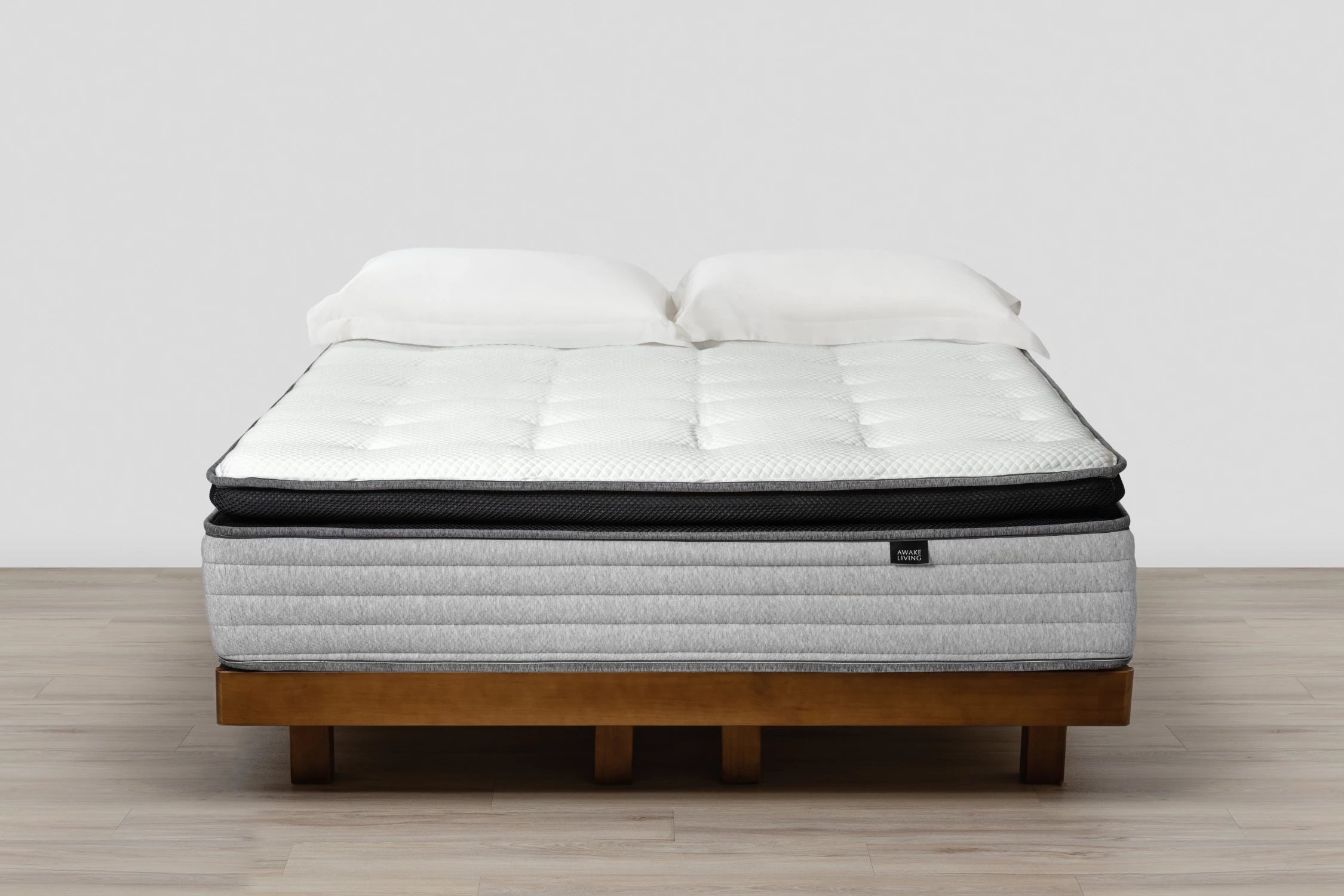 Premium 2.3 零壓深眠床墊擺放於木質床架上,床面鋪有兩顆白色枕頭,呈現平整舒適的狀態。白色立體菱格紋天絲表布與黑色透氣網布中層相互搭配,下方為灰色橫紋側邊設計,整體線條層次分明,營造出現代感與放鬆氛圍兼具的寧靜臥室空間。