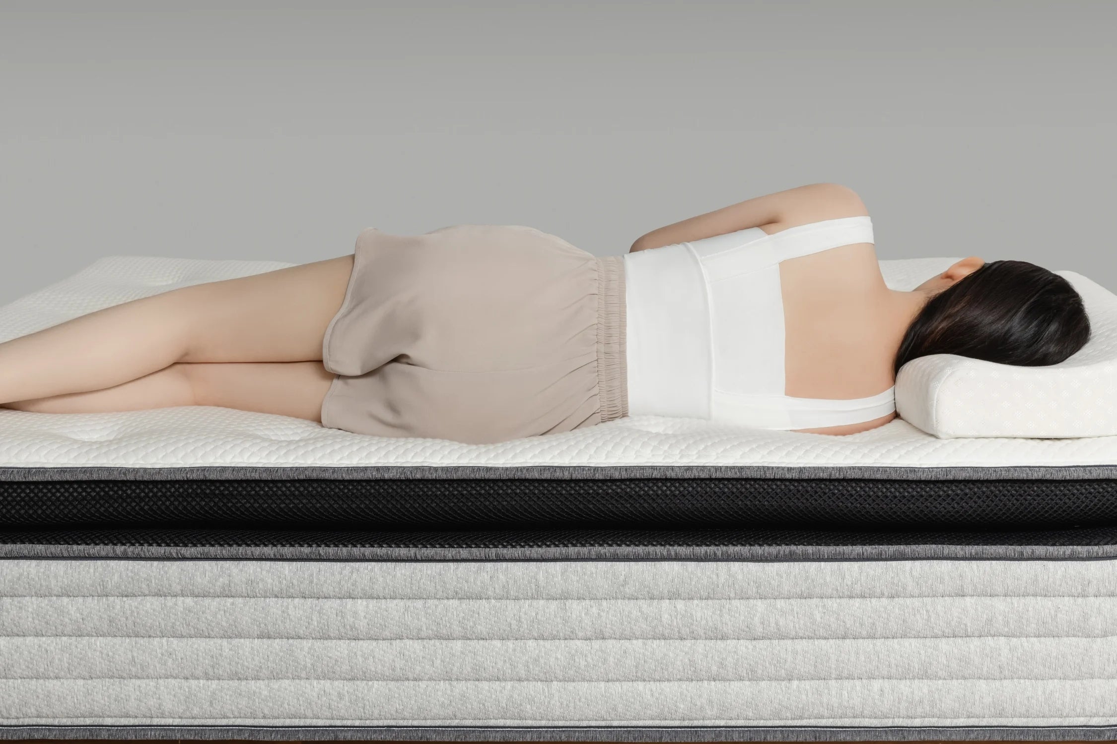 女子側躺在 Premium 2.3 零壓深眠床墊上,身體自然貼合床面,展現床墊優異的釋壓支撐特性。白色立體菱格天絲表布與中層黑色透氣網布營造出清新舒適的視覺質感,搭配柔灰色混紡床沿與穩重床架,整體氛圍靜謐安穩,呈現深層放鬆的睡眠體驗。