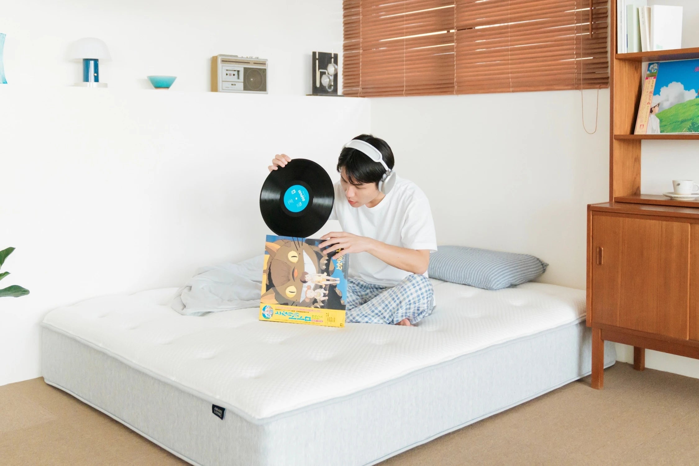 一位戴著耳機的男子坐在 Elite 2.0 床墊上,手上拿著一張黑膠唱片。