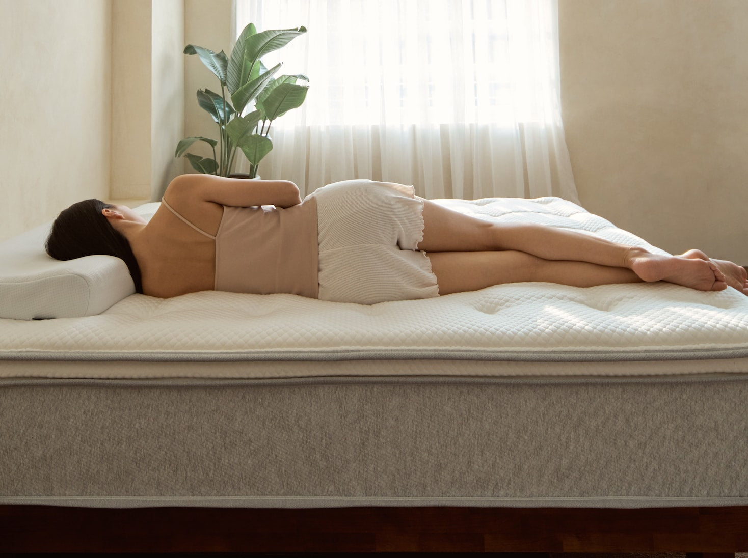 一位女性身著睡衣躺在覺醒家居 Original 經典好眠床墊上，頭枕著覺醒家居冰峰涼感枕，呈現出床墊良好的支撐力
