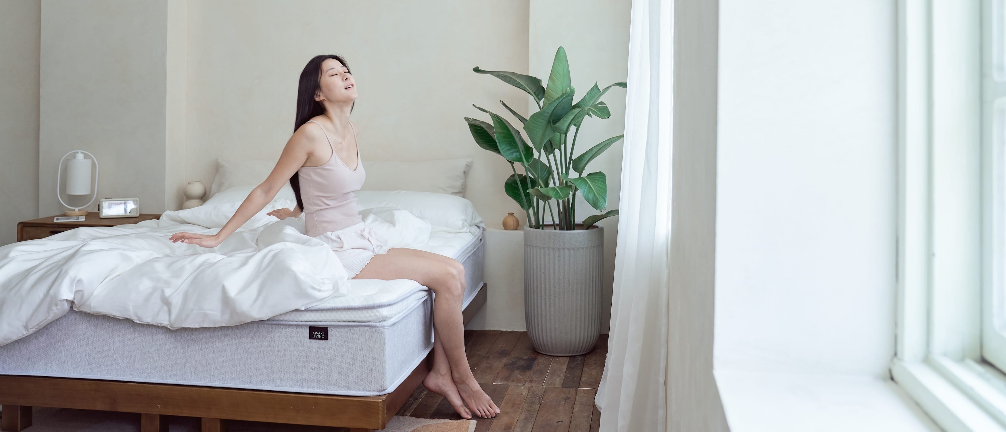 一位女性坐在覺醒家居 Original 經典好眠床沿露出滿意的笑容迎接美好的早晨 - 桌機版本照片