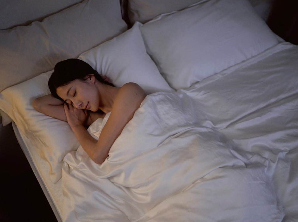 在一個燈光昏暗的空間，一位女性睡在覺醒家居的 Original 經典好眠床墊上露出滿意的睡眠微笑