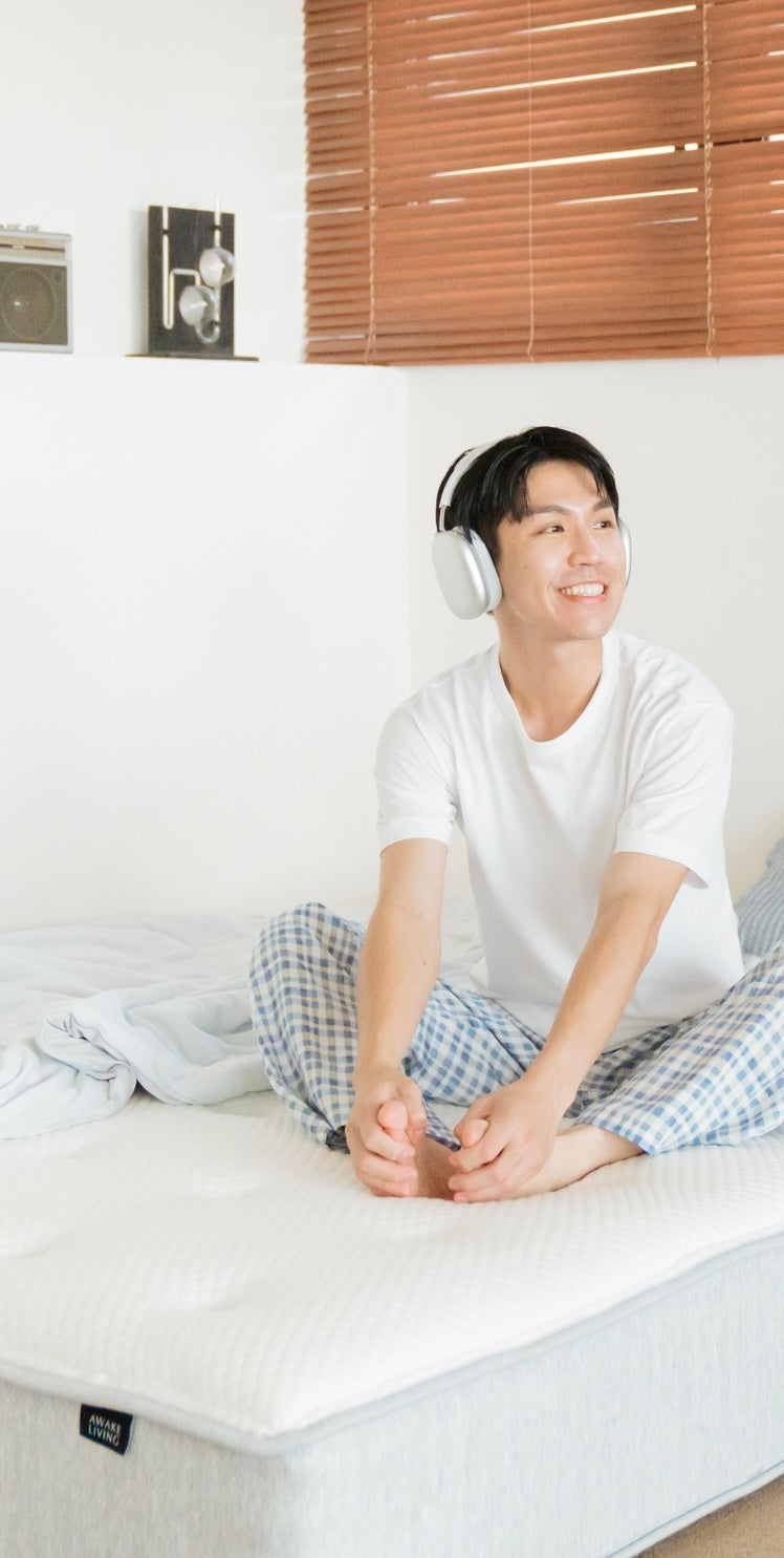 男子身著睡衣帶著耳機坐在覺醒家居的床墊上