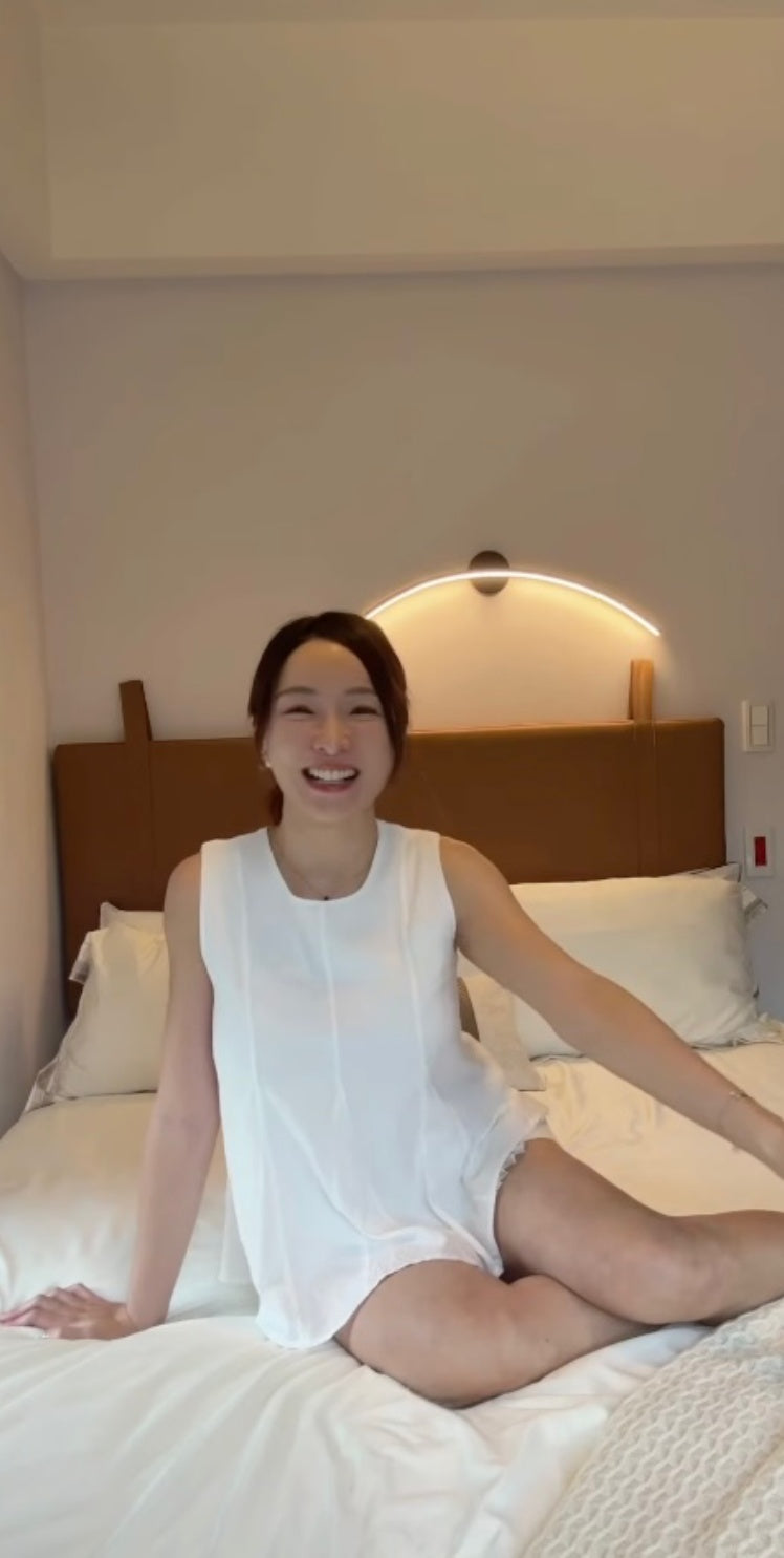 一位女性坐在床上，在有著弧形設計的床頭燈前開懷大笑。