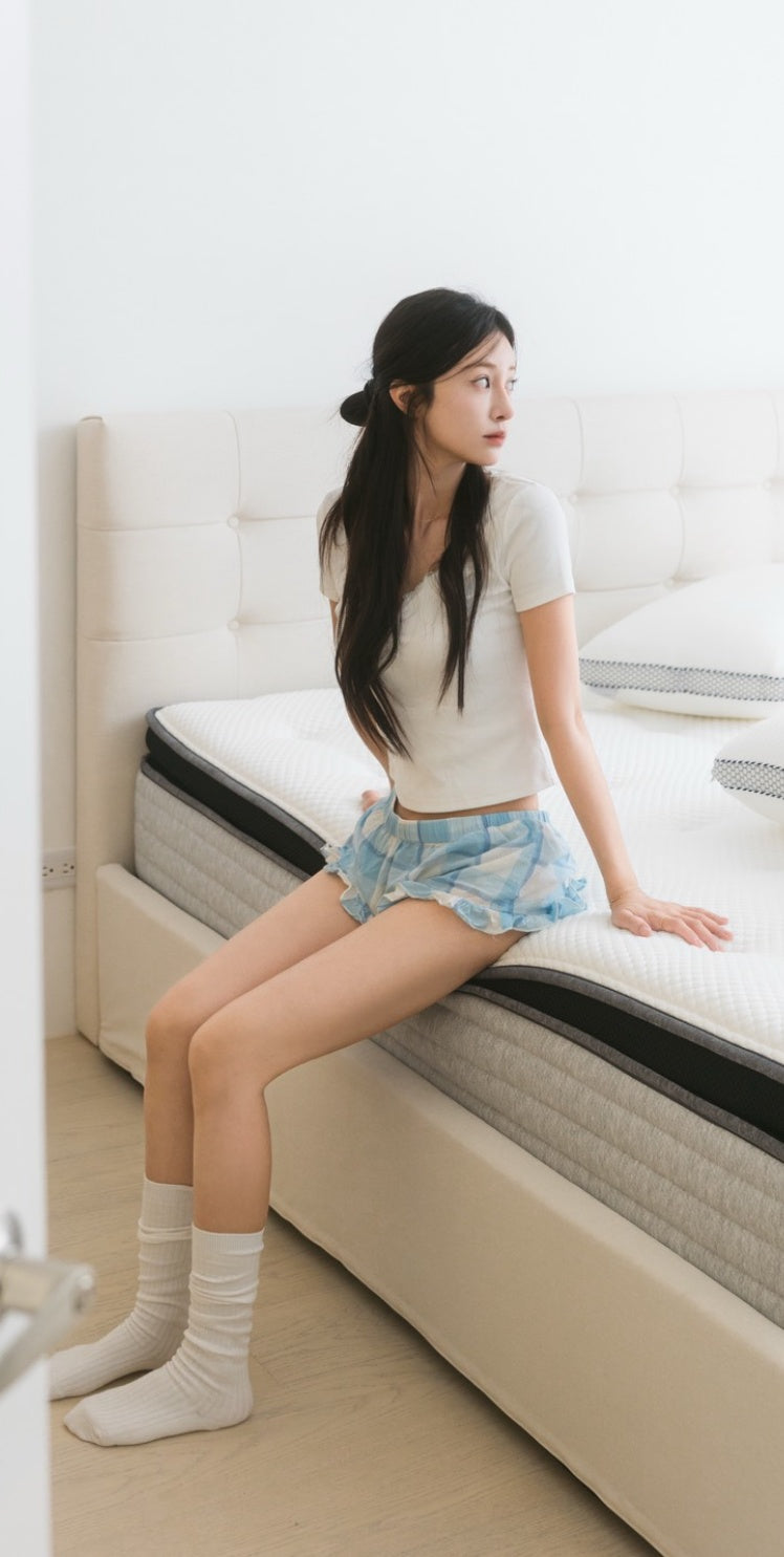 一位長髮女性坐在床沿，回頭望向一旁，身下的床墊有著灰色的床邊設計。
